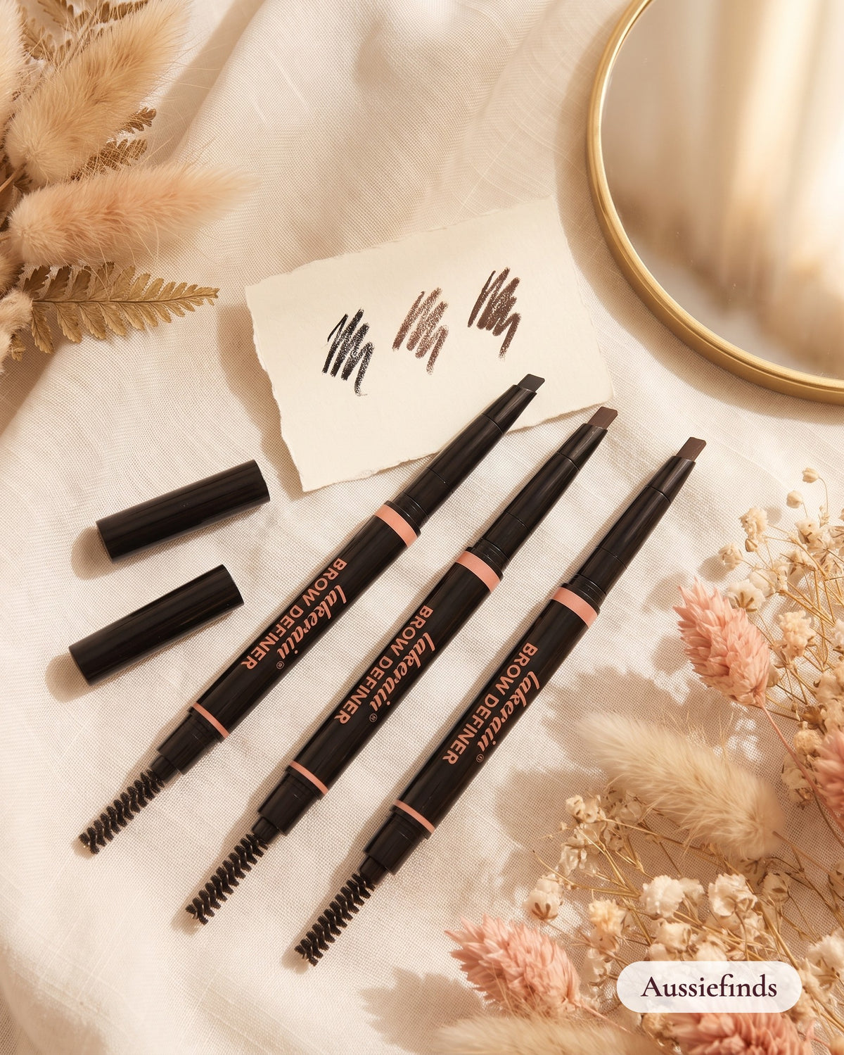 2-in-1 Brow Pencil in three shades with spoolie brush, flat lay on linen