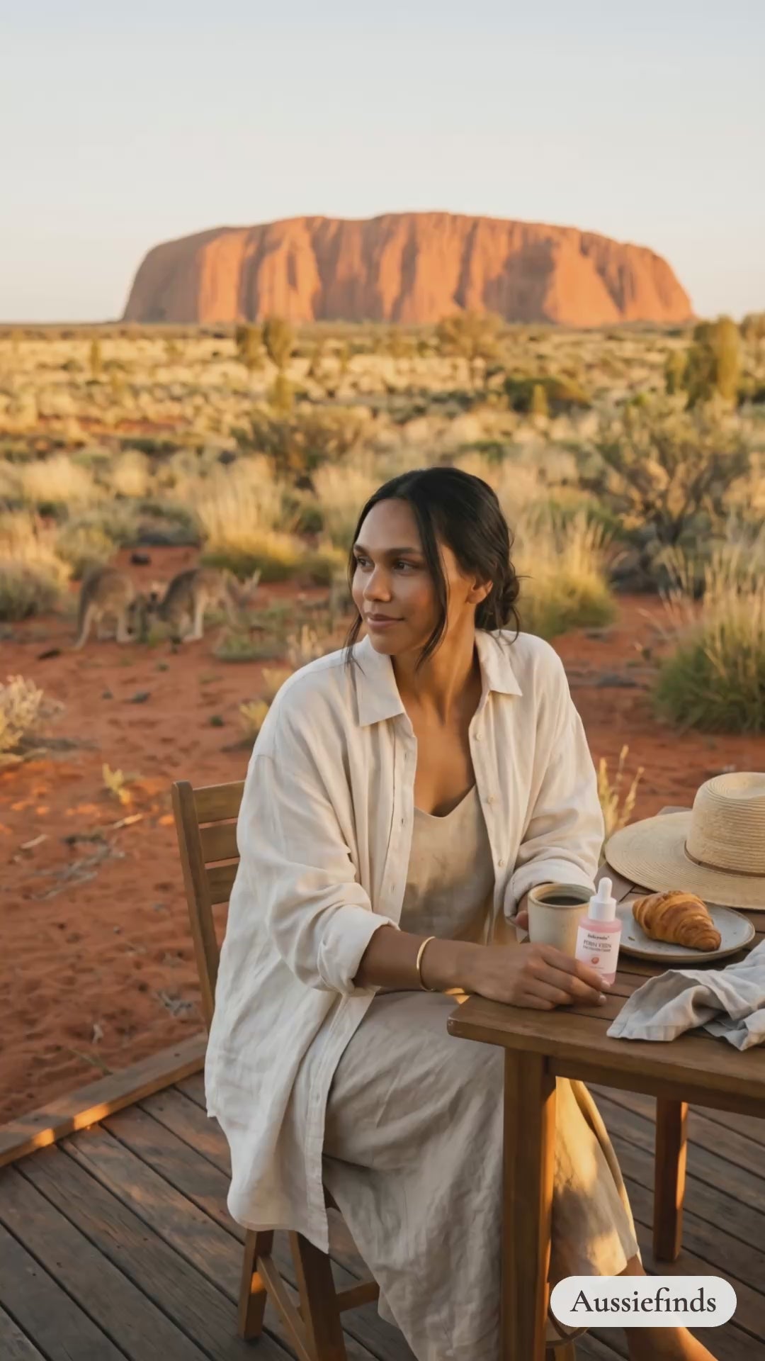 Model holding the PDRN Pink Peptide Serum at sunrise in front of Uluru